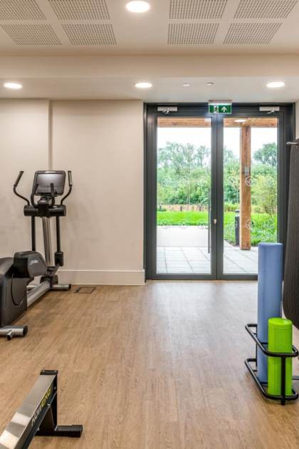 A gym room with exercise equipment, including treadmills, exercise bikes, kettlebells, medicine balls, and stability balls. A glass door provides a view of an outdoor area.