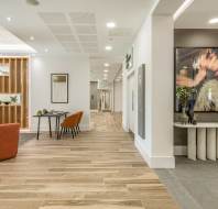 Modern interior with wooden flooring and minimalist decor. Features a lounge area with orange chairs, a desk with a chair, and abstract art on the walls.