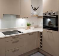 Modern kitchen with beige cabinets, electric stovetop, and built-in oven. Countertop holds decor items. Recessed lighting provides illumination.