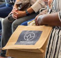 Person holding a reusable Mayfield-branded tote bag while sitting among others.