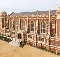 A large, ornate red-brick building with arched windows, decorative stonework, and towers, viewed from above on a clear day.