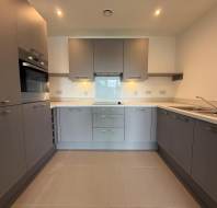 Modern kitchen with grey cabinets, built-in oven, electric cooktop, under-cabinet lighting, and a stainless steel sink on the right, shown in a clean, uncluttered state.