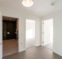 A bright, modern room with wood flooring, three open white doors leading to a bathroom and other rooms, white walls, and a ceiling light.