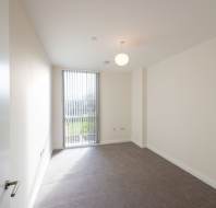 Empty room with beige walls, grey carpet, a ceiling light, vertical blinds on a window, and electrical outlets on the right wall.