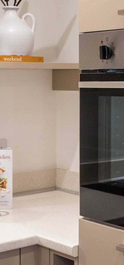 Modern kitchen corner with a built-in oven, light countertops, a cookbook, potted plant, and ceramic containers.