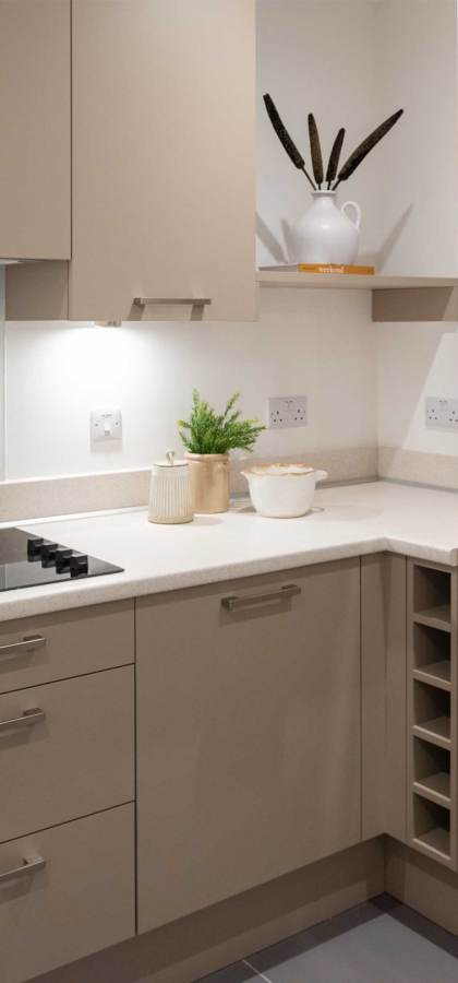 Modern kitchen with beige cabinets, electric stovetop, and built-in oven. Countertop holds decor items. Recessed lighting provides illumination.