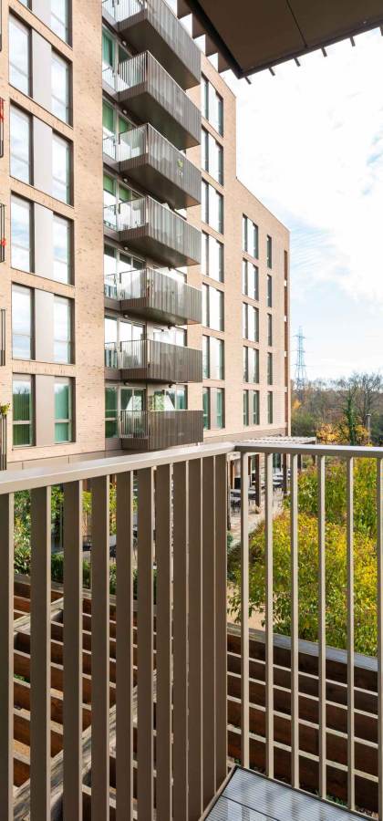 View from a balcony overlooking modern apartment buildings, a landscaped courtyard, and a green lawn with trees in the background.
