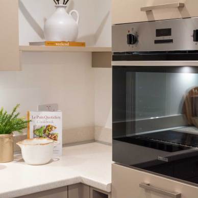 Modern kitchen corner with a built-in oven, light countertops, a cookbook, potted plant, and ceramic containers.