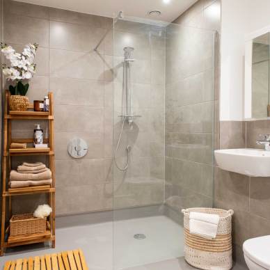 Modern bathroom with a glass-enclosed shower, wooden shelf with towels and toiletries, a sink, and a toilet.