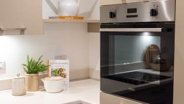 Modern kitchen corner with a built-in oven, light countertops, a cookbook, potted plant, and ceramic containers.