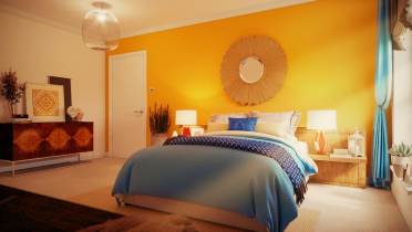 A cozy bedroom with a yellow accent wall, sunburst mirror, white door, wooden and blue bedding, bedside lamps, and a chest of drawers with various decor items.